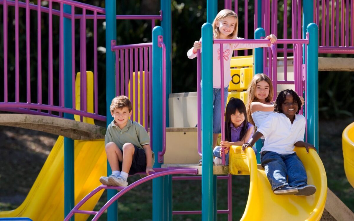 A group of diverse children enjoying playground slides on a sunny day outdoors.