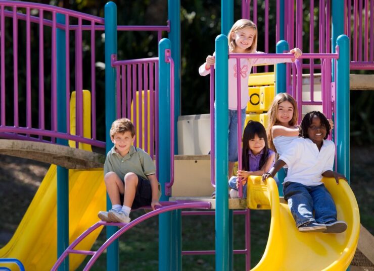A group of diverse children enjoying playground slides on a sunny day outdoors.