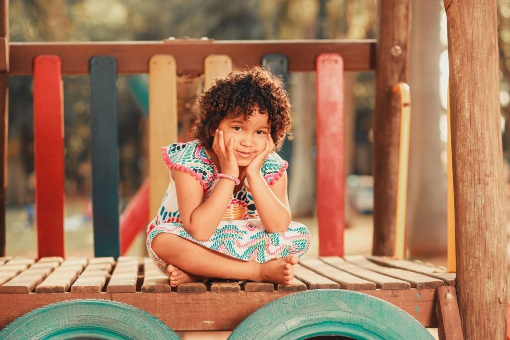 Smiling child with curly hair sitting on a vibrant playground structure, embodying joy and playfulness.