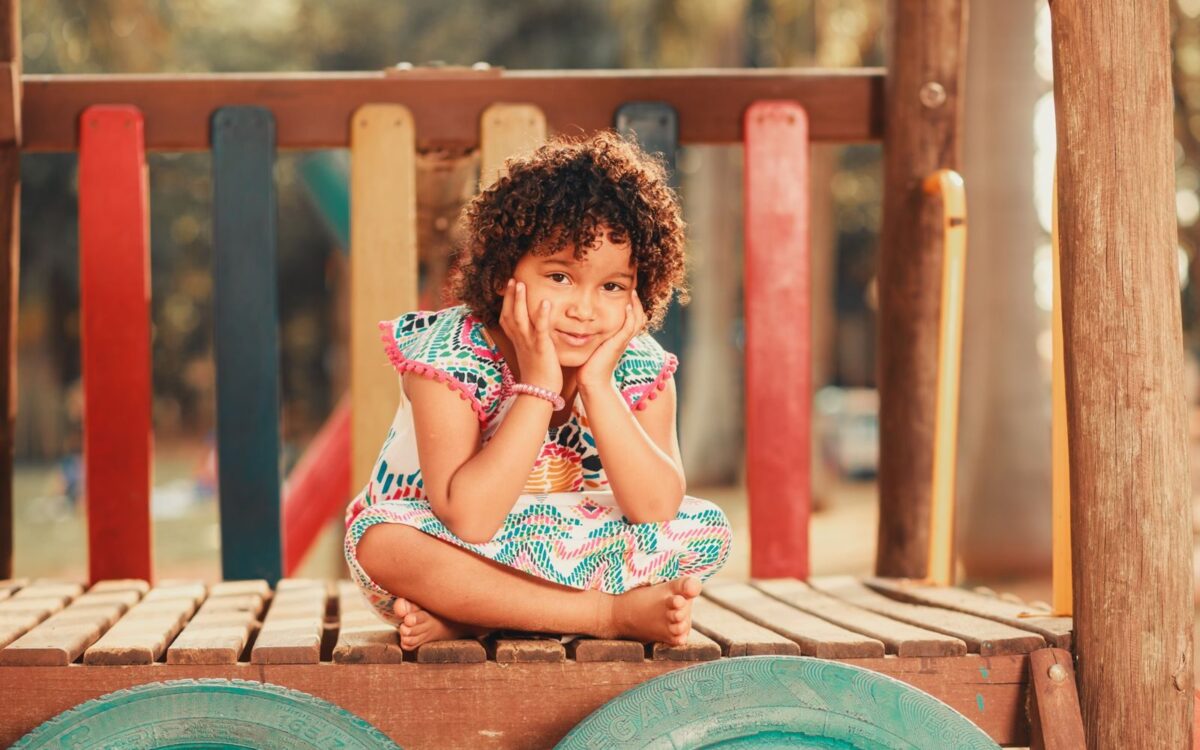 Smiling child with curly hair sitting on a vibrant playground structure, embodying joy and playfulness.