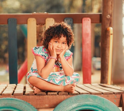 Smiling child with curly hair sitting on a vibrant playground structure, embodying joy and playfulness.