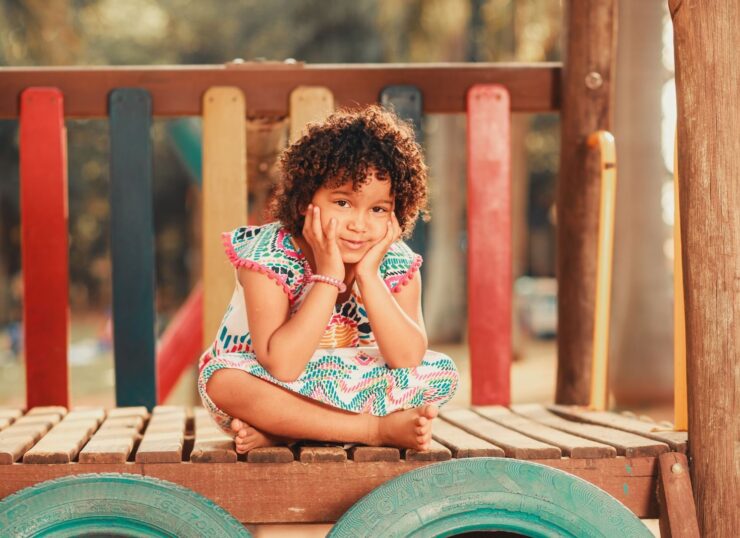 Smiling child with curly hair sitting on a vibrant playground structure, embodying joy and playfulness.