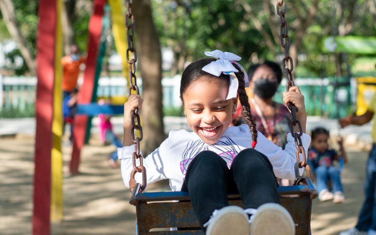 Smiling young girl with braided hair enjoying a swing ride outdoors.