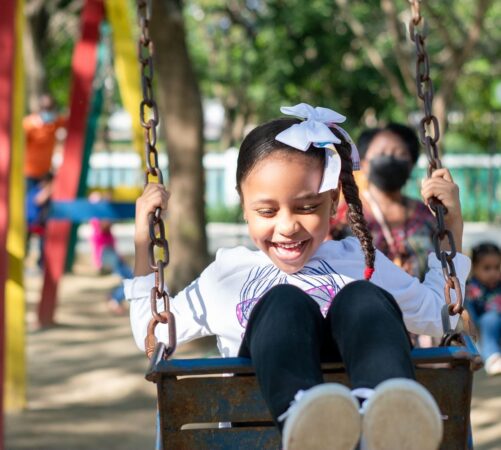 Smiling young girl with braided hair enjoying a swing ride outdoors.